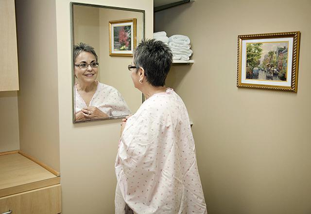 patient wearing hospital gown looks at self in mirror