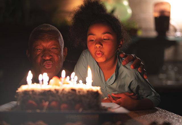 girl helps grandfather blow out birthday candles